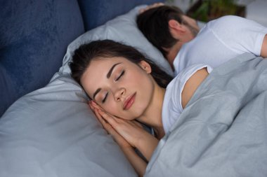 Young woman sleeping by her husband in bed  clipart