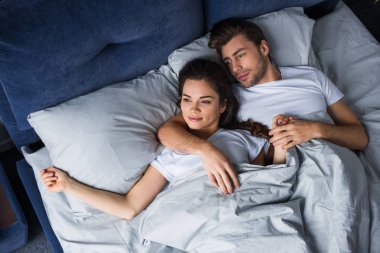 Smiling couple tenderly embracing while lying in bed clipart