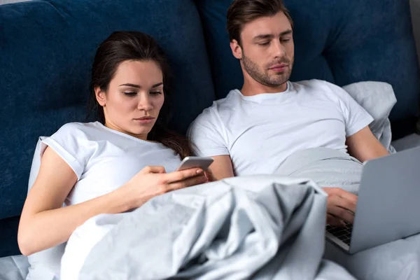 男子和妇女使用数字设备 而躺在床上 — 图库照片