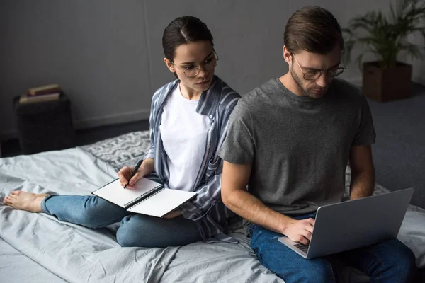 Mulher Escrevendo Bloco Notas Olhando Para Homem Trabalhando Laptop Enquanto — Fotografia de Stock