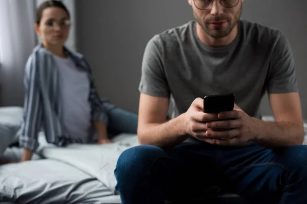 Mulher Olhando Para Homem Sentado Cama Usando Smartphone — Fotografia de Stock