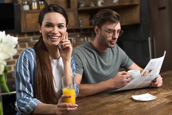 コーヒーを飲んだり 新聞を読む男ながら電話で話しているジュースのガラスを笑顔の女性 — ストック写真