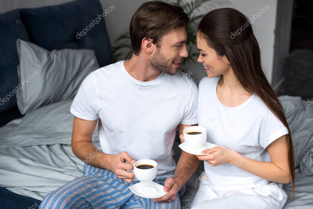 Smiling wife and husband drinking coffee in bed