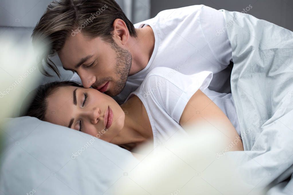 Husband tenderly kissing sleeping wife in bed