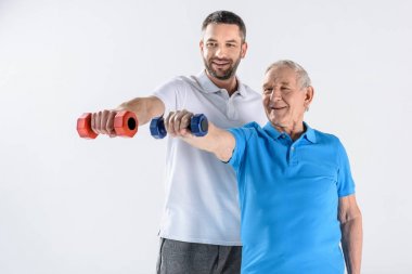 Rehabilitasyon terapist ve komuta sizde dumbbells ile egzersiz gülümseyen portresi gri izole