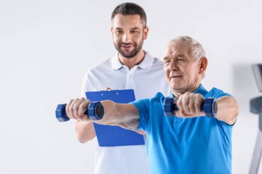 Komuta sizde gri zemin üzerinde dumbbells ile egzersiz yardımcı Not Defteri ile rehabilitasyon terapist portresi