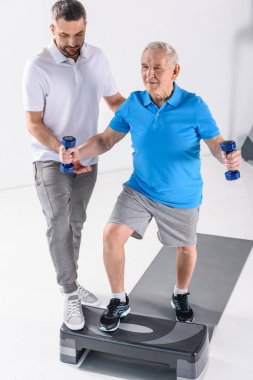 Komuta sizde Step gri zemin üzerinde üzerinde dumbbells ile egzersiz yardımcı rehabilitasyon terapist