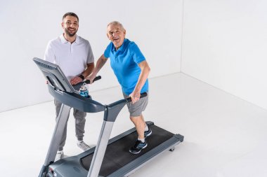 high angle view of rehabilitation therapist assisting senior man exercising on treadmill  clipart