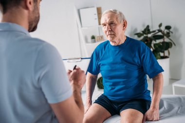 Rehabilitasyon terapistin masaj masasında not defteri ve kıdemli adamla kırpılmış atış