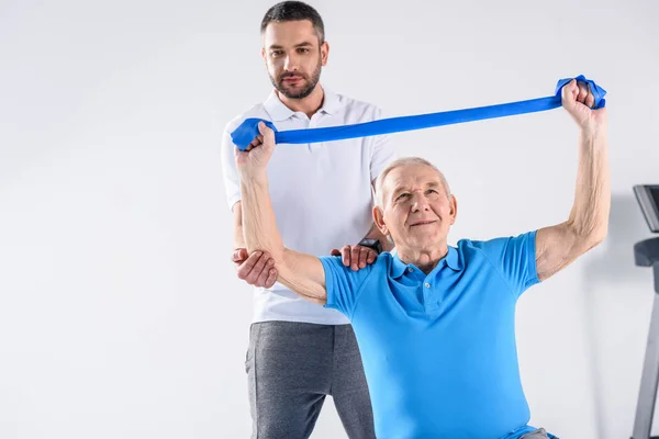 Porträtt Rehabilitering Terapeut Hjälpa Ledande Man Tränar Med Gummi Band — Stockfoto