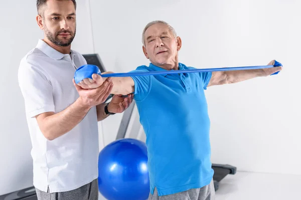 Portret Rehabilitacji Terapeuta Pomoc Starszy Człowiek Ćwiczenia Taśmą Gumową — Zdjęcie stockowe