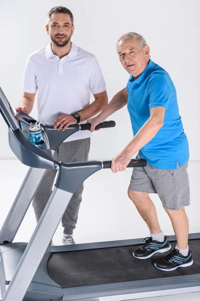 康复治疗师和老人在跑步机上的灰色隔离 — 图库照片