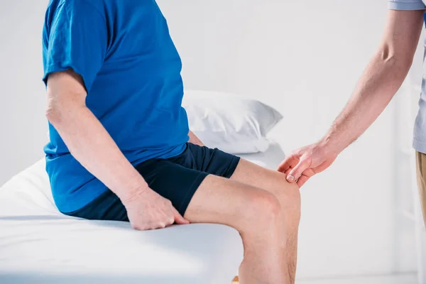 Tiro Recortado Del Terapeuta Rehabilitación Comprobar Rodilla Del Hombre Mayor — Foto de Stock