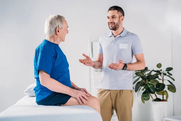 Sorridente Terapeuta Reabilitação Homem Sênior Mesa Massagem Tendo Conversa — Fotografia de Stock
