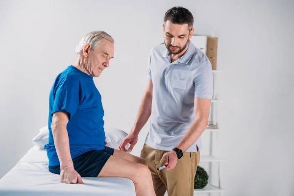 Rehabilitering Terapeut Med Reflex Hammare Kontrollera Senior Mans Knä Massagebänk — Stockfoto