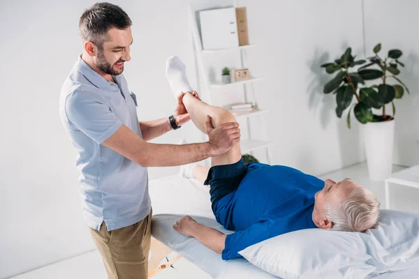 Fisioterapeuta Sorrindo Massageando Perna Homem Sênior Mesa Massagem — Fotografia de Stock