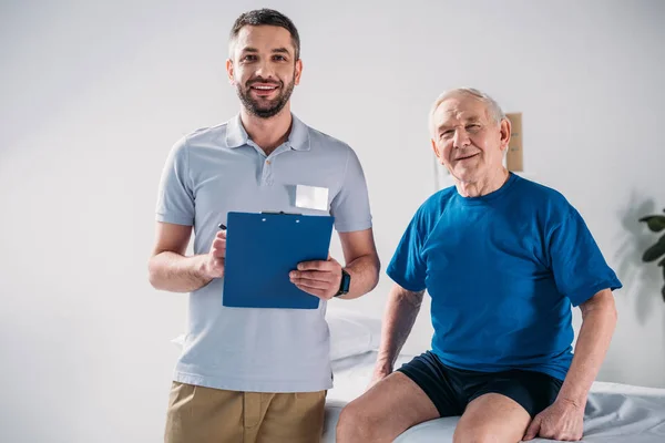 Potret Terapis Rehabilitasi Dengan Notepad Dan Tersenyum Pria Senior Meja — Stok Foto