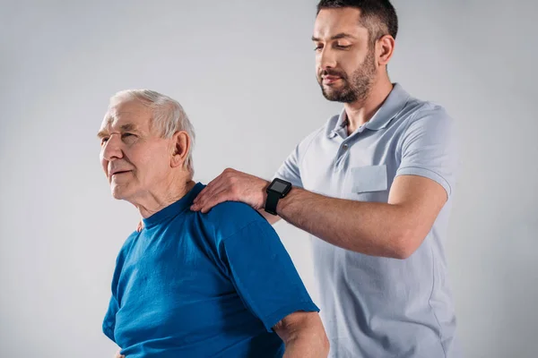 Sjukgymnasten Gör Massage Till Senior Man Isolerade Grå — Stockfoto