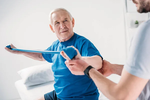 Обрезанный Снимок Реабилитационного Терапевта Помогающего Пожилому Человеку Резиновой Лентой — стоковое фото