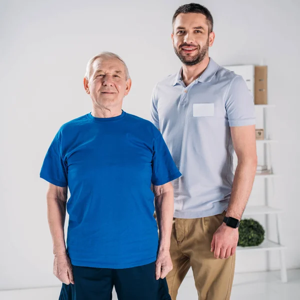 Portrait Smiling Senior Man Rehabilitation Therapist Looking Camera Grey Backdrop — Stock Photo, Image