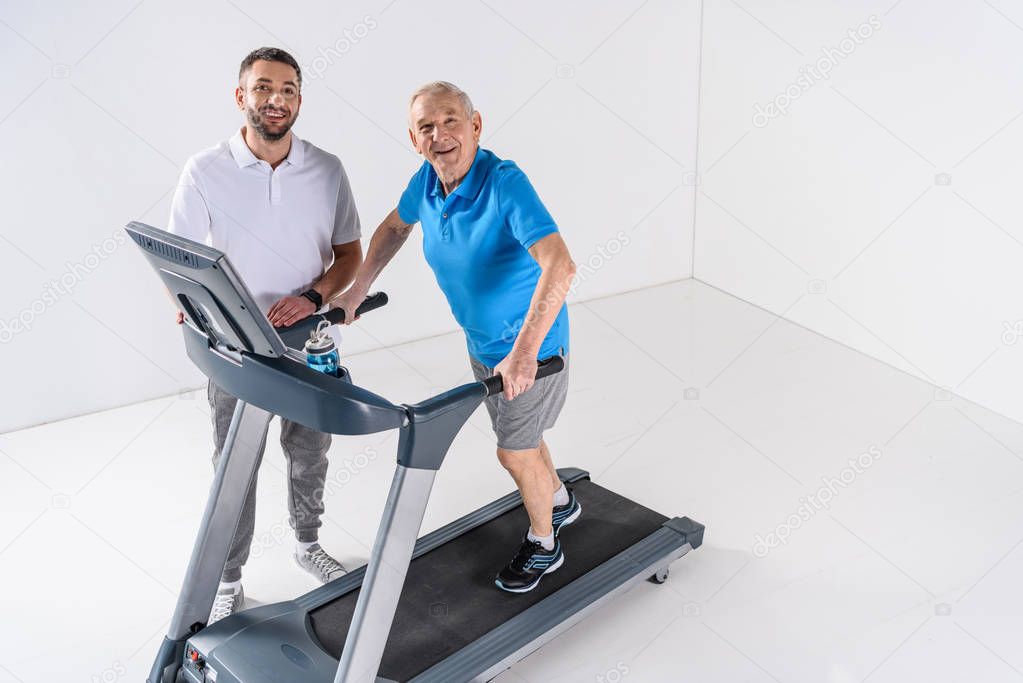 high angle view of rehabilitation therapist assisting senior man exercising on treadmill 