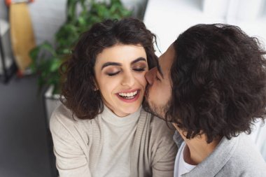 boyfriend kissing smiling girlfriend at home