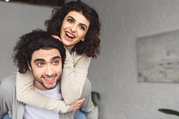 boyfriend giving piggyback to laughing girlfriend at home