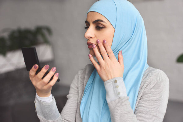beautiful muslim woman in hijab looking at mirror at home