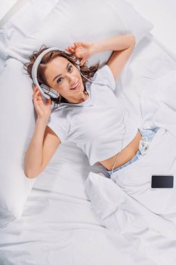 genç gülümseyen kadın yatakta kulaklık müzik dinleme havai görünümü