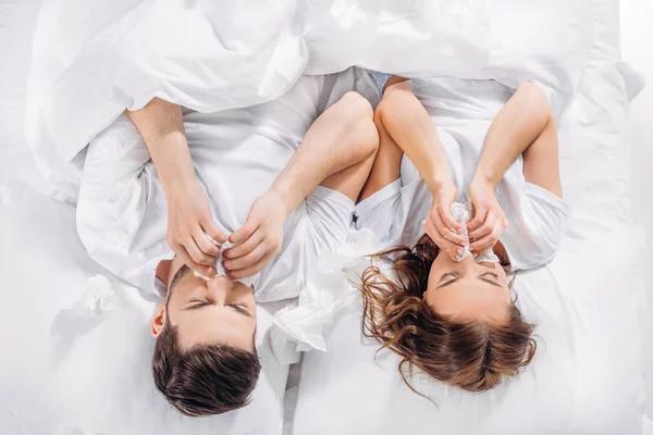 overhead view of couple with tissues lying in bed while having cold