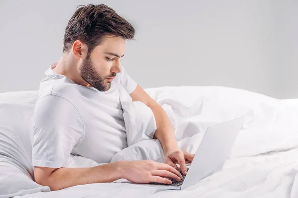 Sidovy Fokuserad Skäggig Man Använder Laptop Sängen Isolerad Grå — Stockfoto