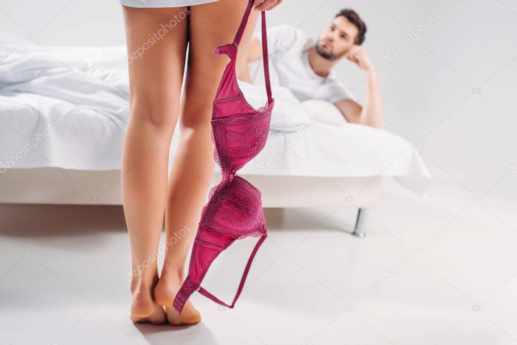 selective focus of woman with bra in hand and boyfriend lying on bed