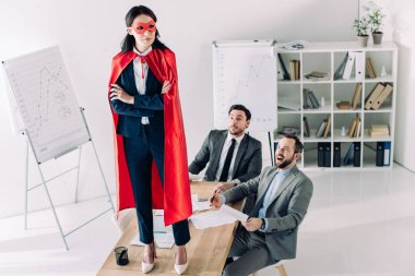 super businesswoman in mask and cape standing on table in office  clipart
