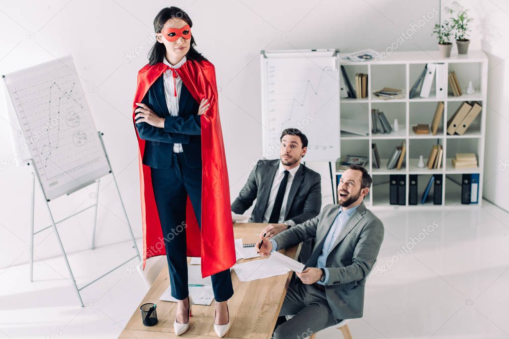 super businesswoman in mask and cape standing on table in office 