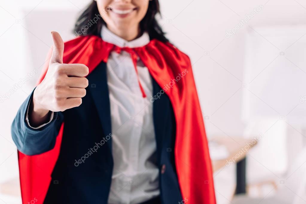 cropped image of super businesswoman in cape showing thumb up in office