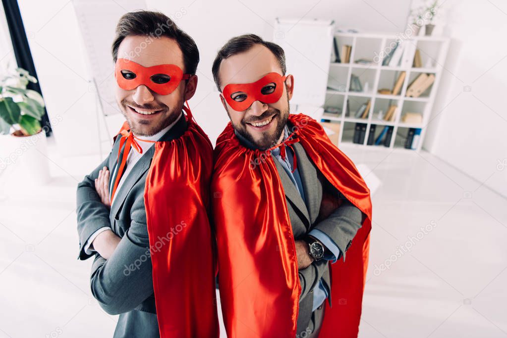 high angle view of smiling handsome super businessmen in masks and capes with crossed arms in office