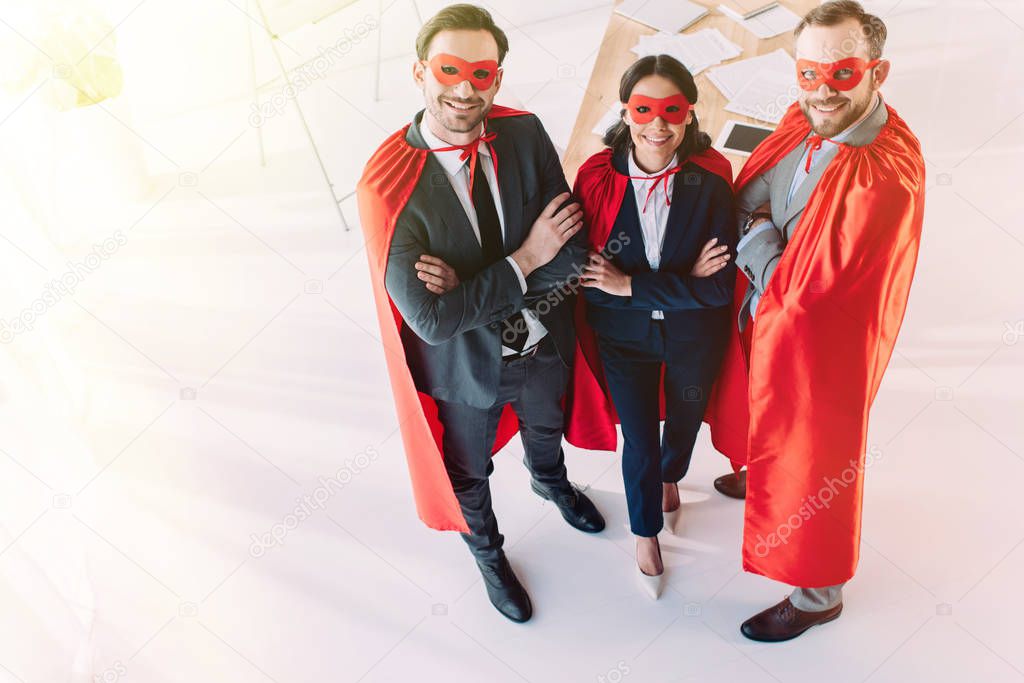 high angle view of super businesspeople in masks and capes with crossed arms looking at camera in office