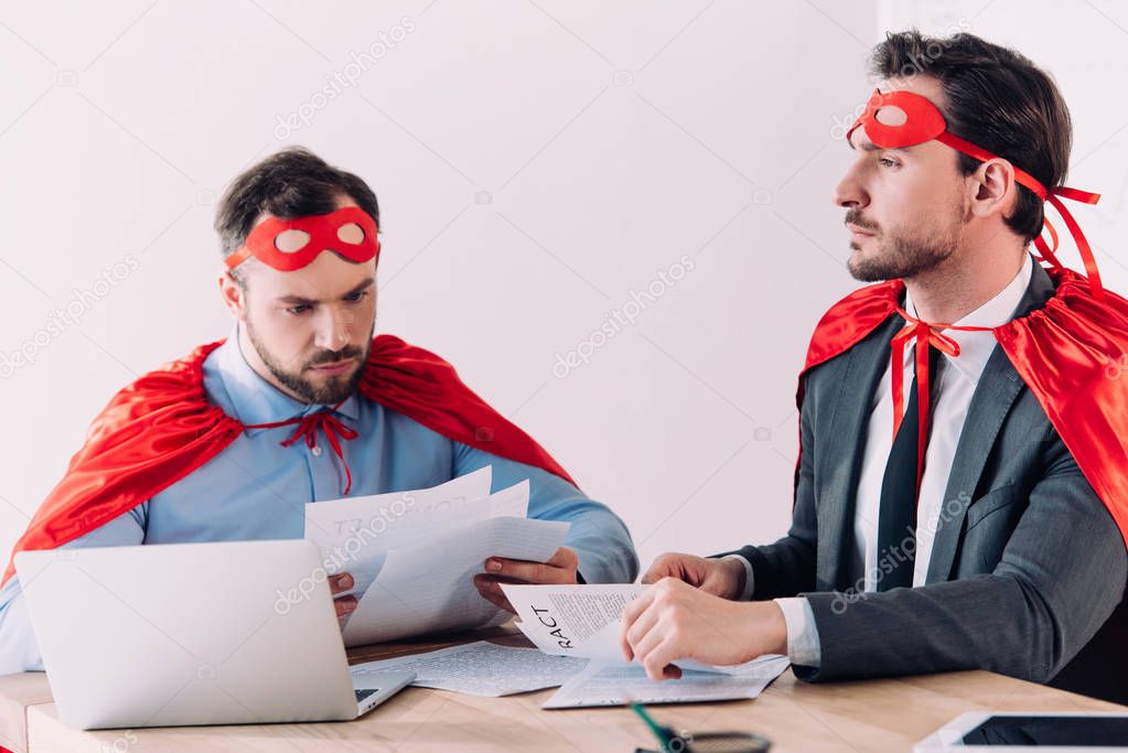 handsome super businessmen in masks and capes working with documents in office