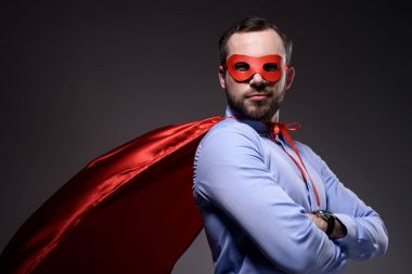 handsome super businessman in mask and cape with crossed arms looking at camera isolated on black clipart