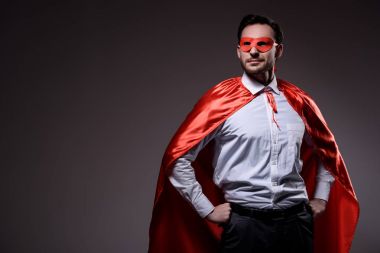 handsome super businessman in mask and cape standing with hands akimbo isolated on black clipart