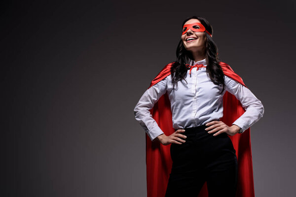 smiling attractive super businesswoman in red cape and mask isolated on black