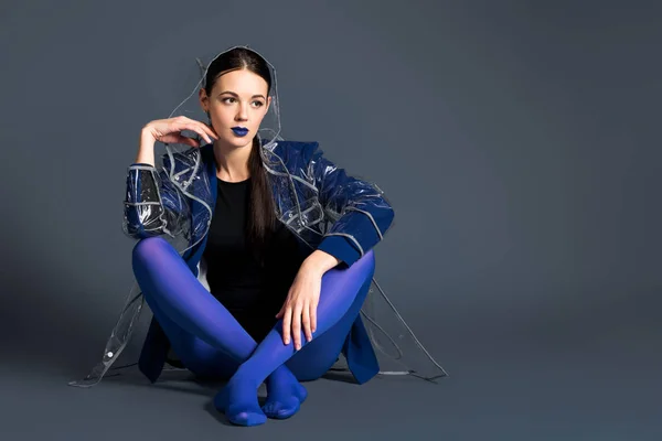 Slim woman in blue pantyhose and raincoat sitting on dark background