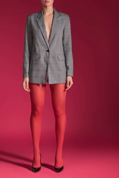 Cropped view of woman wearing red tights and grey jacket on red background