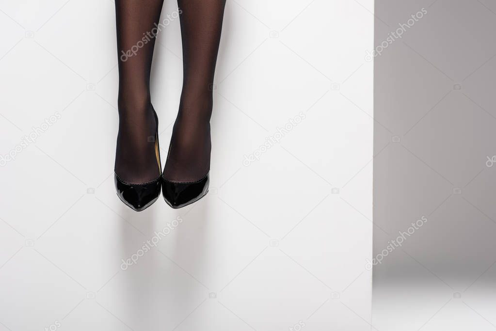 Female legs in black pantyhose and shoes on white background
