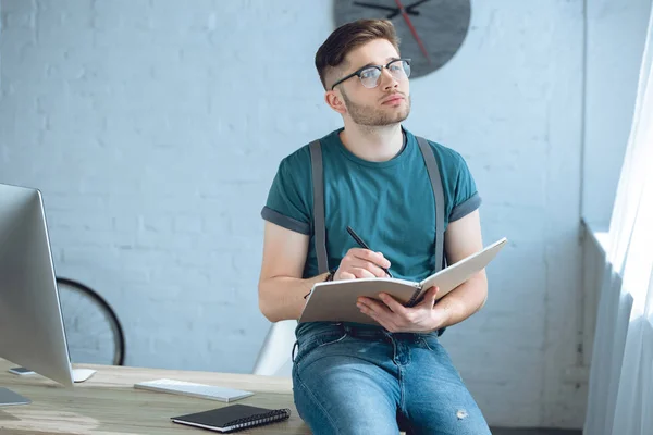 Pensive Young Man Eyeglasses Looking Away While Writing Notebook Home — Stock Photo, Image