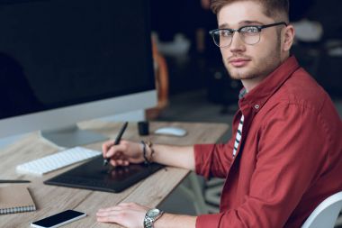 Bilgisayar ve grafik tablet içeren tablo başına oturmuş sakallı adam