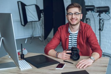 Çalışma tablosu tarafından kamera ve grafik tablet ile oturan mutlu freelancer adam