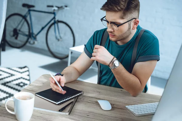 Νεαρός Άνδρας Γυαλιά Χρησιμοποιώντας Smartphone Ενώ Εργάζεστε Στο Σπίτι Γραφείο — Δωρεάν Φωτογραφία