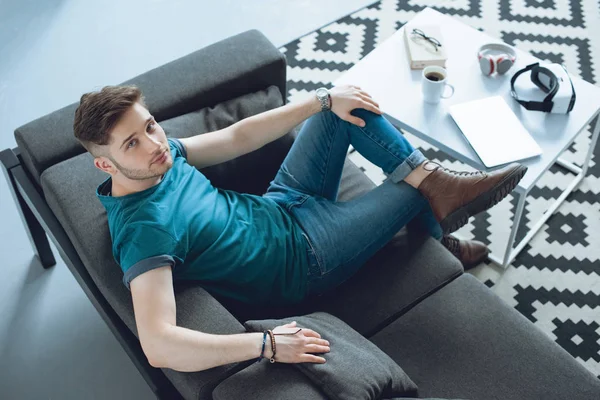 Yakışıklı Genç Adam Kanepede Oturan Kameraya Bakarak Yüksek Açılı Görünüş — Ücretsiz Stok Fotoğraf