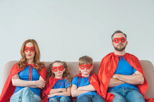 super family in masks and cloaks sitting with crossed arms and looking at camera on grey